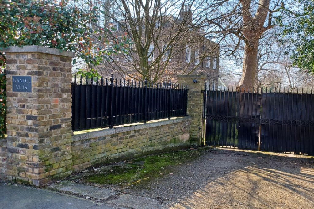 Brick wall and black iron gates outside Wandle Villa with trees in the background.