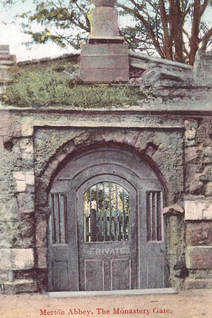 A vintage image of a medieval gateway at Merton Priory, featuring a stone arch and wooden door, photographed around 1920.