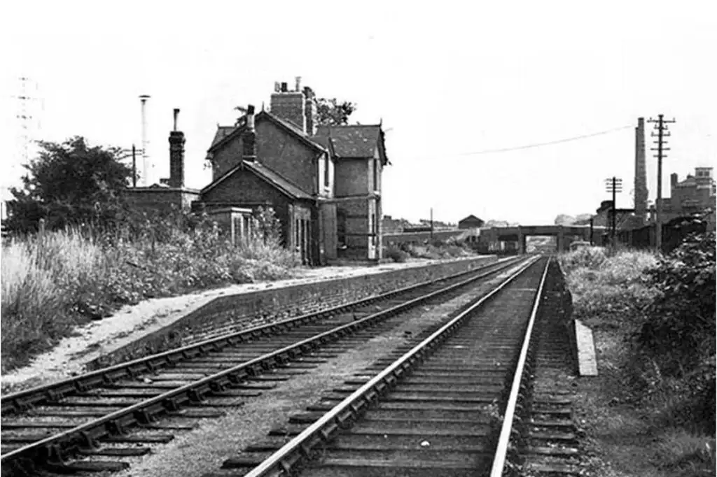 Historic black and white photograph of Merton Abbey Railway Station, showing railway tracks, station buildings, and industrial structures in the background.